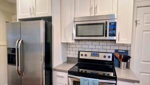 A kitchen with stainless steel appliances, white cabinetry, and a tiled backsplash. - ​The Seattle Scenes House: 5-Suite Boutique Home near Light Rail (Seattle)