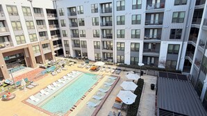 Um edifício com vários andares e uma área de piscina no terraço, incluindo espreguiçadeiras e guarda-sóis.