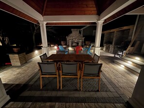An outdoor patio with a wooden table and chairs, a stone fireplace, and a stone wall. - 4-bedroom house with beautiful backyard patio perfect for relaxing stays. (Frankford)