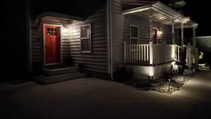 Ein Haus mit roter Tür, einer Veranda mit Geländer und einem kleinen Garten.