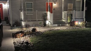 Ein zweistöckiges Haus mit einer Veranda, einer roten Tür und einem gut beleuchteten Weg.