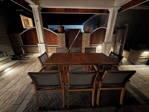 An outdoor dining area with a wooden table and chairs, surrounded by stone walls and a brick floor. - 4-bedroom house with beautiful backyard patio perfect for relaxing stays. (Frankford)