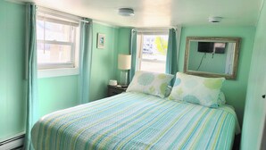 A room with a bed, a nightstand, a lamp, a window with curtains, and a wall-mounted TV. - Cozy 1 bed/1 bath two blocks from beach and boards (North Wildwood)