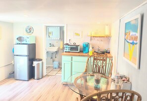 Cocina compacta con refrigerador, microondas y tostadora. En primer plano, una mesa de comedor con sillas.