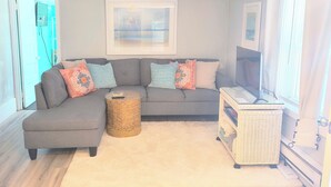 A living room with a grey sectional sofa, a round wicker side table, a flat-screen TV, and a wicker storage unit. - Cozy 1 bed/1 bath two blocks from beach and boards (North Wildwood)