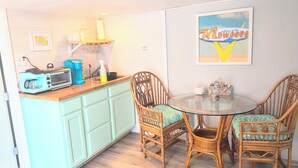 A kitchen with a toaster, coffee maker, and a glass of water on the counter. There is a dining table with wicker chairs and a framed sign on the wall. - Cozy 1 bed/1 bath two blocks from beach and boards (North Wildwood)