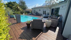 Eine Holzterrasse mit Pool, Gartenmöbeln und Topfpflanzen.