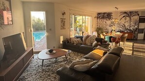 Ein modernes Wohnzimmer mit Fernseher, Sofa, Couchtisch und Essbereich mit Blick auf einen Pool.