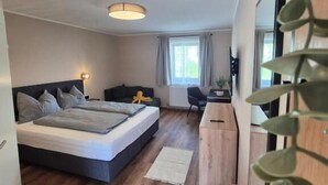 A modern bedroom with a bed, bedside table, desk, chair, and a plant. - Lindengut (Natternbach)