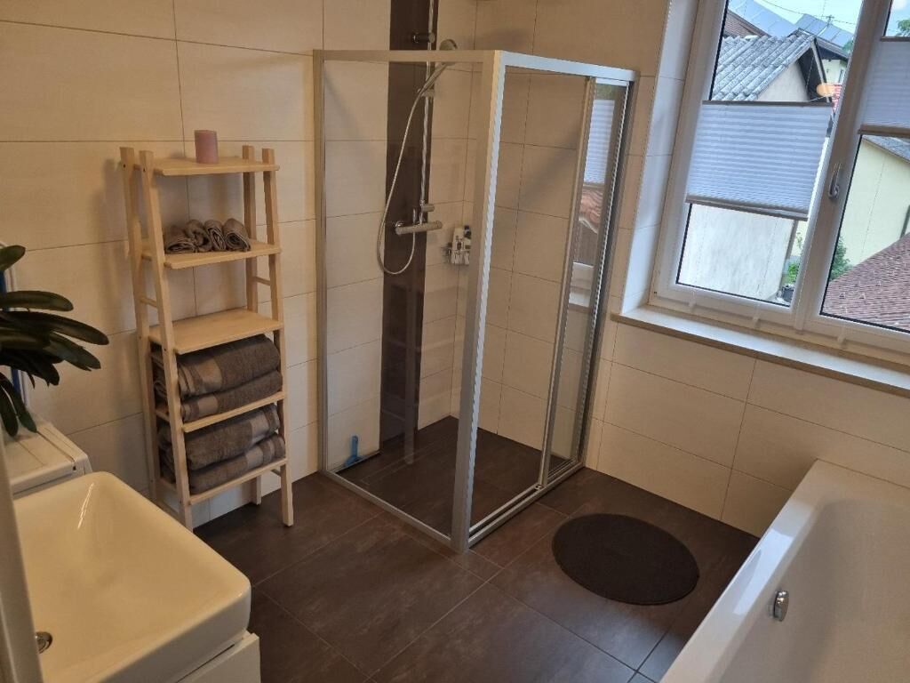 Ein Badezimmer mit Dusche, Waschbecken, Ablage für Handtücher und einem Fenster.