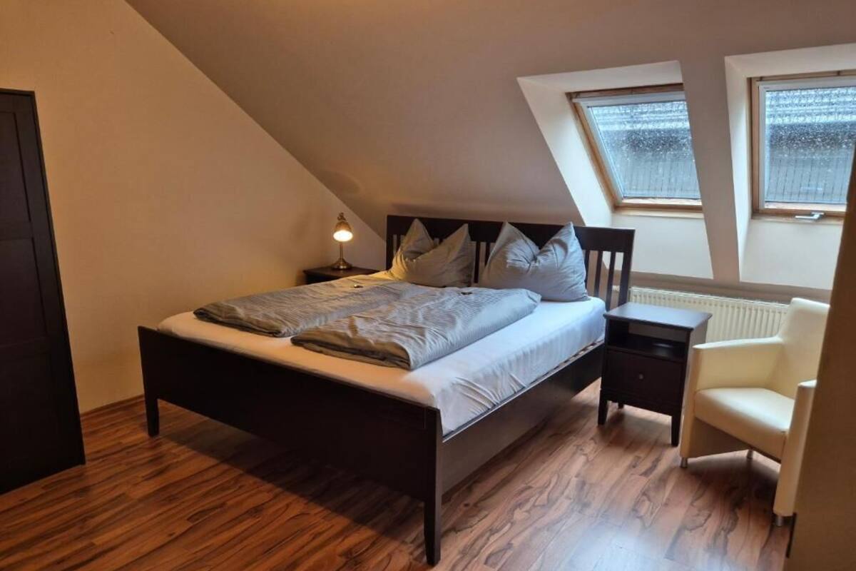 A bedroom with a sloped ceiling, a bed, a nightstand, a chair, and two windows.