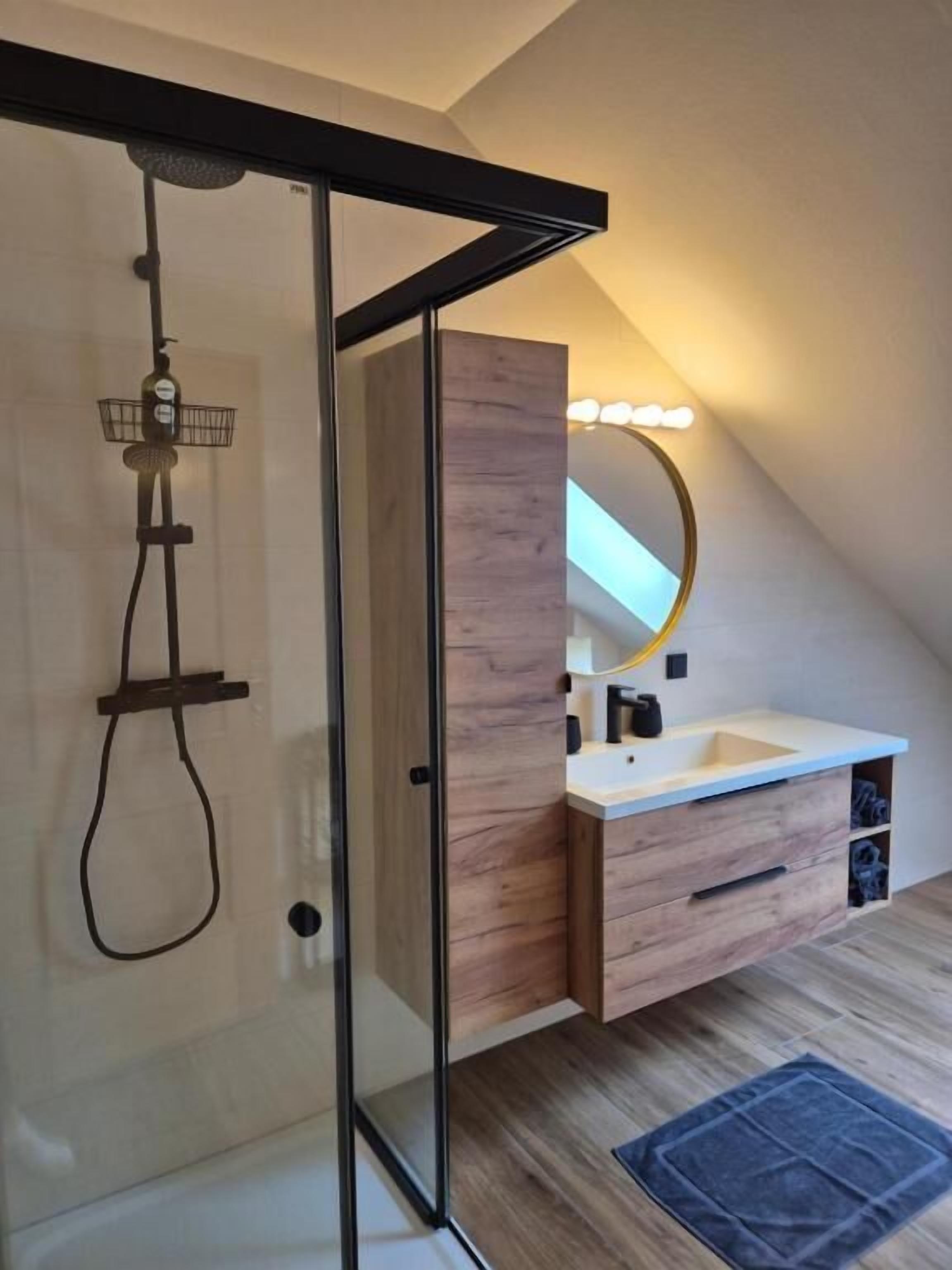 A modern bathroom with a glass shower enclosure, a wooden vanity with a mirror, and a small sink.