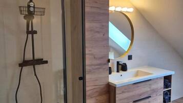 A modern bathroom with a glass shower enclosure, a wooden vanity with a mirror, and a small sink.
