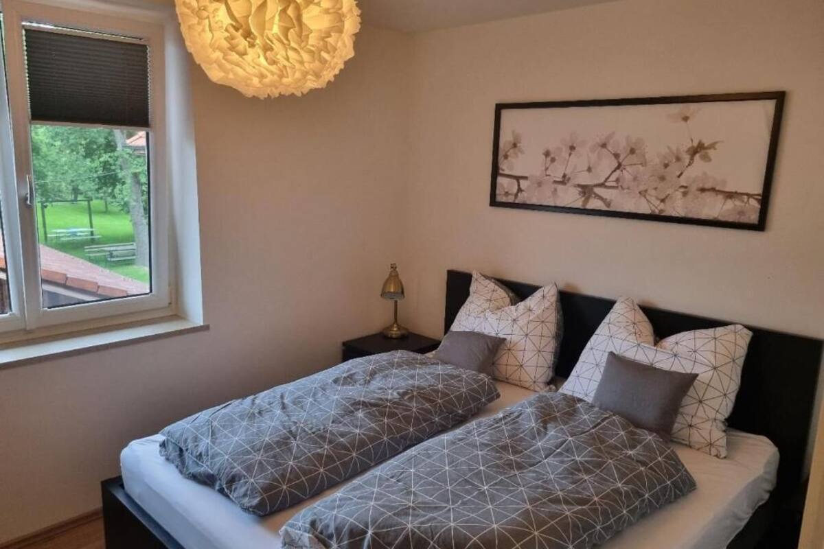 A double bed with geometric patterned bedding, a wall-mounted picture, and a hanging light fixture.