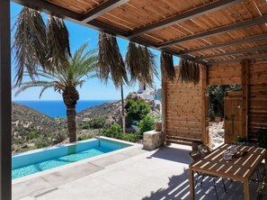 Une piscine avec vue sur la mer, une pergola en bois et une table avec des chaises.