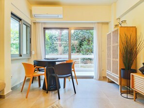 A dining area with a table and chairs, a potted plant, and a view of greenery outside. - Vibrant Flat in Voula Center (Voula)