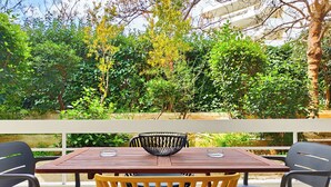 Eine Terrasse im Freien mit einem Holztisch und Stühlen, umgeben von üppigem Grün und einem weißen Geländer.