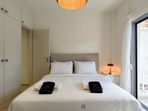 A hotel room with a bed, two pillows, a nightstand with a lamp, and a window with curtains. - Vibrant Flat in Voula Center (Voula)