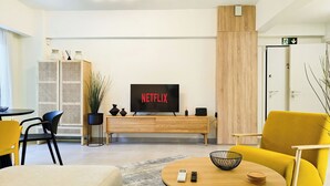 Ein modernes Wohnzimmer mit Flachbildfernseher, einer Couch, einem Couchtisch und einem Essbereich mit Stühlen.