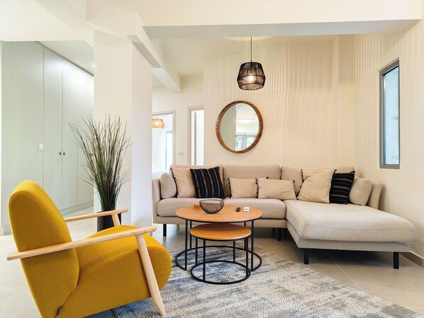 A modern living room with a sofa, a yellow chair, a round mirror, and a hanging light fixture. - Vibrant Flat in Voula Center (Voula)