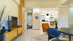 Ein modernes Wohnzimmer mit Fernseher, einer hölzernen Bank und einem Essbereich mit Stühlen.