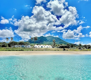 Un hôtel situé en bord de mer, avec une chaîne de montagnes en toile de fond, un ciel bleu azur et une eau turquoise.