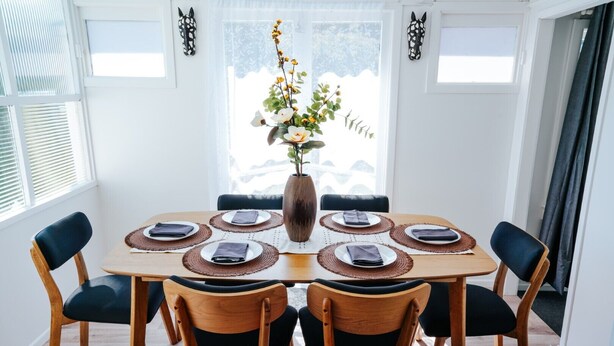 Spisebord med seks stole, en vase med blomster og udsigt til det fri.
