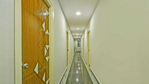 Corredor com porta de madeira à esquerda, piso de azulejos e um hall que leva a um quarto com janela.