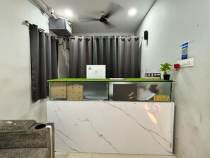 A reception area with a marble counter, grey curtains, a ceiling fan, and a small potted plant. - Hotel O Madhapur - Borabanda (Hyderabad)