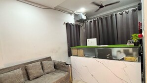 Quarto com sofá, pequena escrivaninha com um laptop, ventoinha no teto e cortina.
