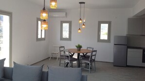 A modern kitchen with a built-in refrigerator, a dining area with a round table and chairs, and pendant lights. - Liopi Village Andros B (Ormos Korthiou)