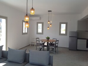 A modern kitchen with a built-in refrigerator, a dining area with a round table and chairs, and pendant lights. - Liopi Village Andros B (Ormos Korthiou)