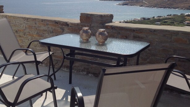 A table with two vases, a chair, and a view of the sea and hills. - Liopi Village Andros B (Ormos Korthiou)