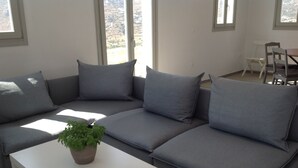 A modern living room with a grey sectional sofa, a white coffee table, and a potted plant. - Liopi Village Andros B (Ormos Korthiou)