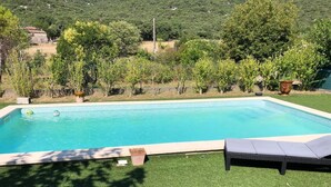 Piscina rectangular con borde de azulejos, rodeada de césped y árboles.