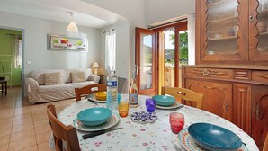 Un comedor con una mesa preparada para cuatro personas, un mueble de madera con puertas de cristal, un sofá y un cuadro enmarcado en la pared.