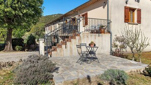 Una casa con un patio de piedra, mobiliario exterior y una escalera que lleva a un balcón.