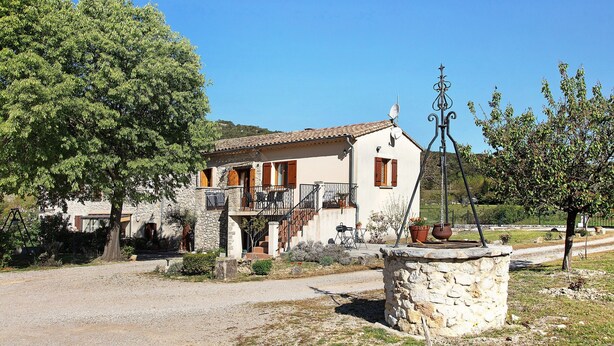 Una casa de piedra con balcón, antena parabólica y camino de entrada de grava.