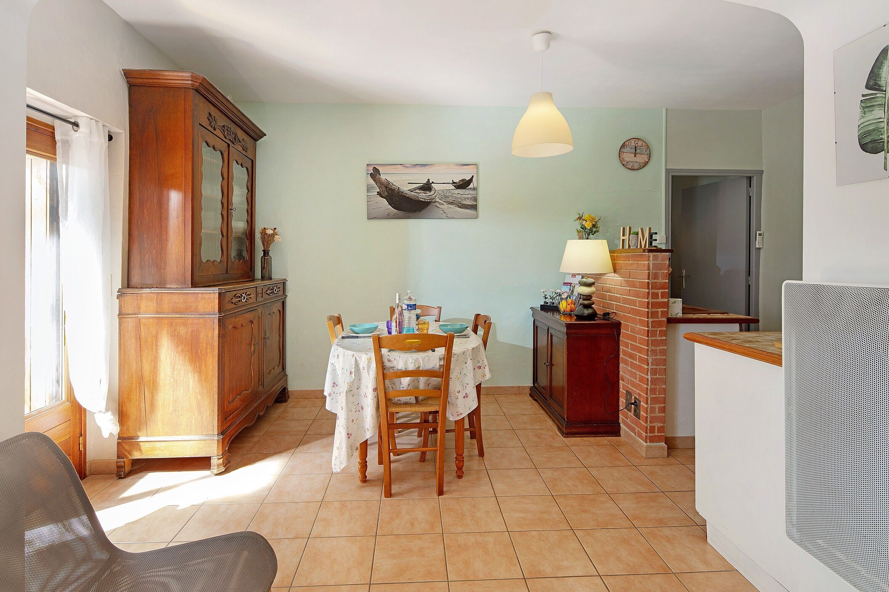 A dining area with a wooden cabinet, a table with chairs, a hanging light fixture, and a painting on the wall.