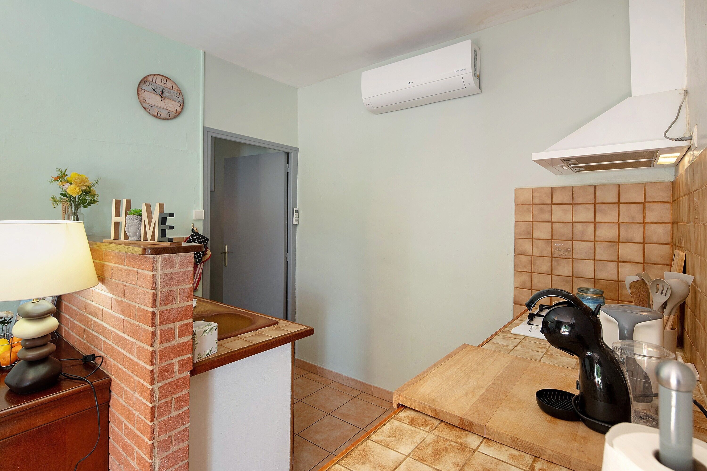 A kitchen with a brick backsplash, a clock, an air conditioner, and a coffee maker.