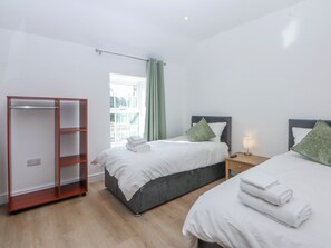 A bedroom with two beds, a wardrobe, a window, and a bedside table with a lamp. - Gate House (Llangefni)