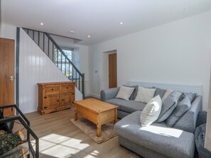 A living room with a staircase, a grey sofa, a wooden coffee table, and a wooden cabinet. - Gate House (Llangefni)