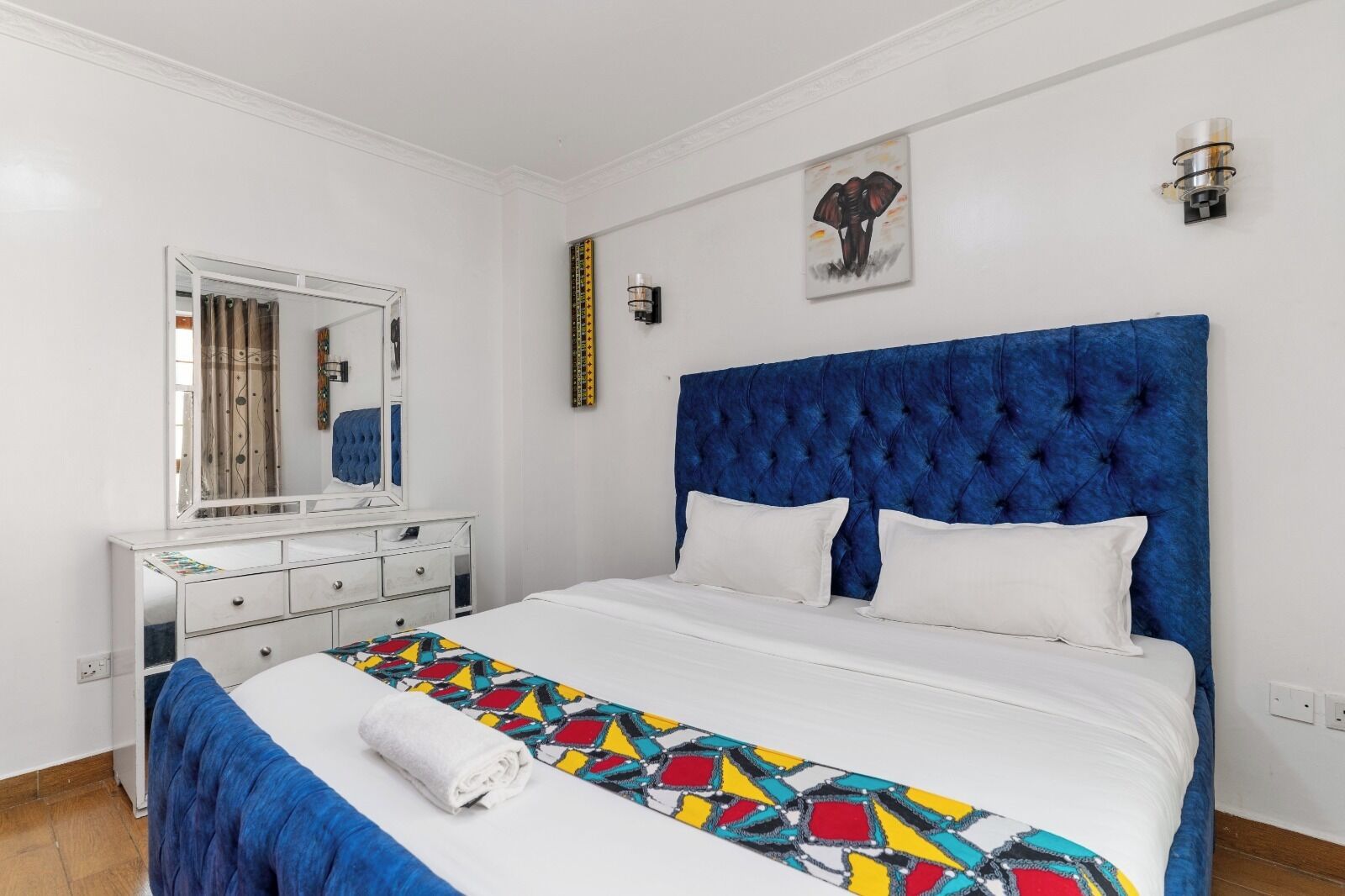 A bedroom with a large bed, a dresser, a mirror, and a wall-mounted light fixture.