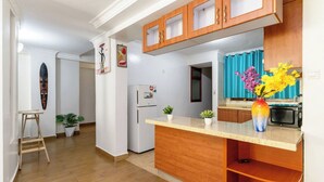 Una cocina con armarios de madera, microondas, refrigerador y una pequeña isla con plantas en macetas.