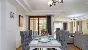 Comedor con una mesa dispuesta para cuatro personas, rodeada de sillas tapizadas, una araña y vistas a través de un ventanal.