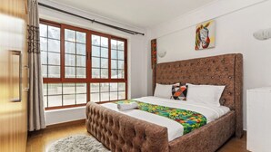 Un dormitorio con un ventanal grande, un cabecero capitonado, una alfombra mullida y una colcha colorida.