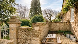Un mur de pierres, un banc en bois et des jardinières en métal dans un espace aménagé en jardin.