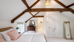 Une chambre avec un plafond en pente, un lit avec des oreillers à rayures, une commode, un miroir et une porte donnant sur une salle de bain.