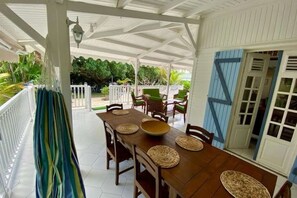 A covered outdoor dining area with a wooden table, chairs, and woven placemats. - Villa Ti' Colibri – Creole Villa with Pool Near the Beach (Saint-François)
