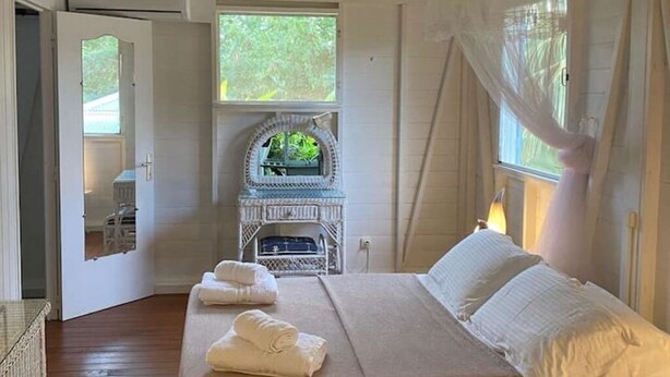 Ein Schlafzimmer mit Bett, kleinem weißem Kamin und Blick auf Grün.